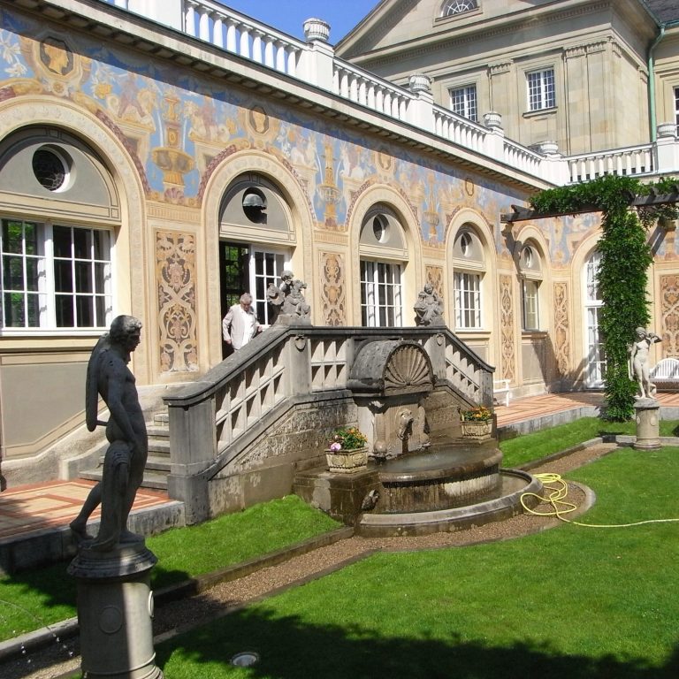 Historisches Gebäude mit außen verzierten Wänden und einem Brunnen im Garten.